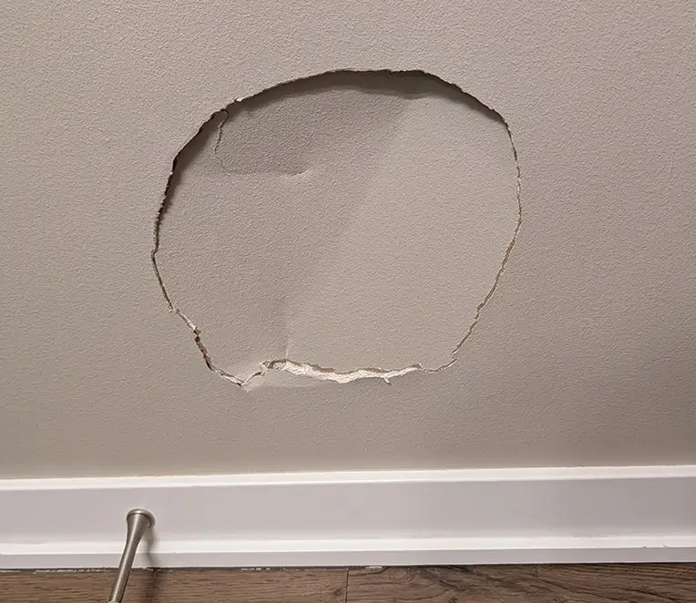 Large damaged section of drywall near the baseboard before wall repair