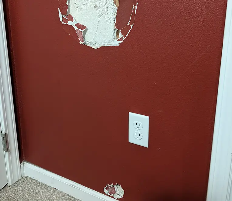 Damaged maroon drywall wall with two holes before repair